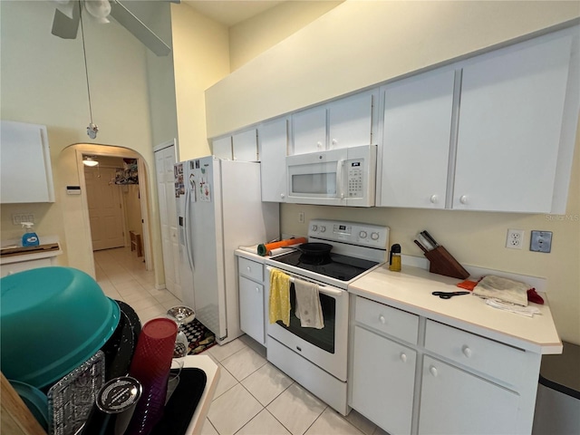 kitchen with white cabinetry, a towering ceiling, light tile patterned flooring, and white appliances