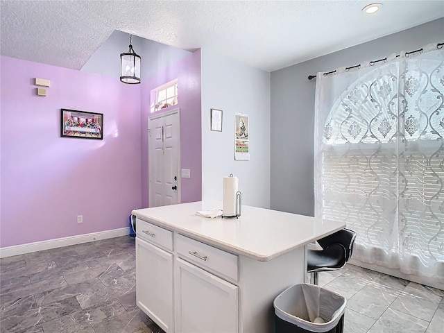 kitchen featuring a textured ceiling, white cabinetry, baseboards, light countertops, and a center island