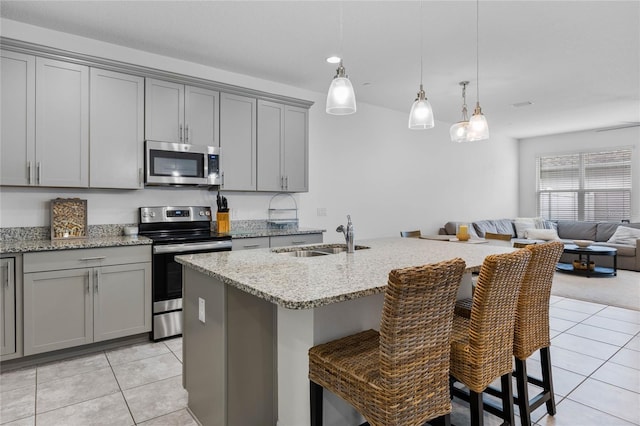 kitchen with sink, a breakfast bar, hanging light fixtures, stainless steel appliances, and an island with sink