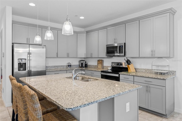 kitchen featuring pendant lighting, sink, a kitchen island with sink, stainless steel appliances, and light stone countertops