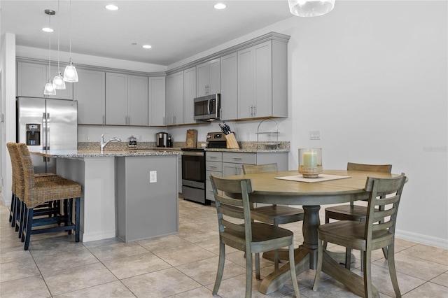 kitchen with light stone counters, appliances with stainless steel finishes, gray cabinets, and hanging light fixtures