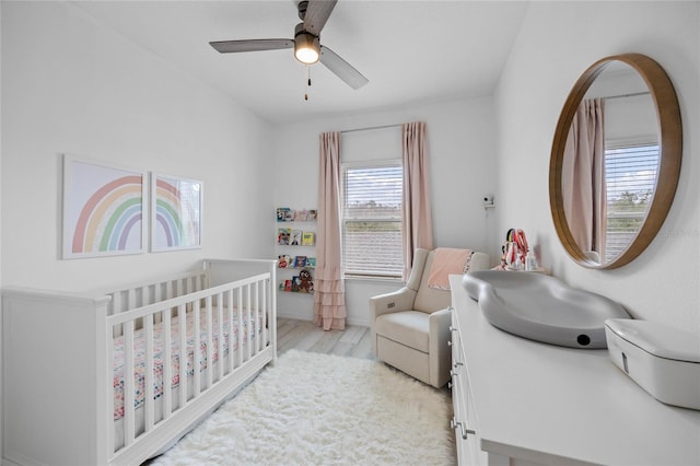 bedroom with a crib, ceiling fan, and light hardwood / wood-style flooring