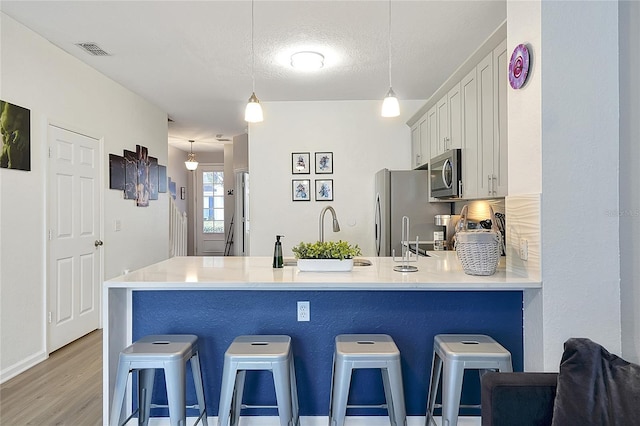 kitchen featuring white cabinetry, decorative light fixtures, a textured ceiling, appliances with stainless steel finishes, and kitchen peninsula