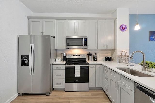 kitchen with pendant lighting, sink, light hardwood / wood-style flooring, appliances with stainless steel finishes, and backsplash