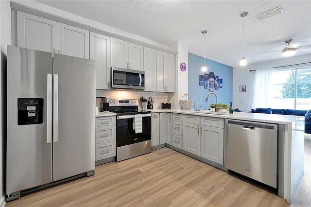 kitchen with decorative light fixtures, sink, kitchen peninsula, stainless steel appliances, and light hardwood / wood-style flooring