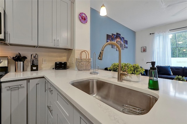 kitchen featuring sink, light stone counters, stainless steel range with electric stovetop, hanging light fixtures, and decorative backsplash