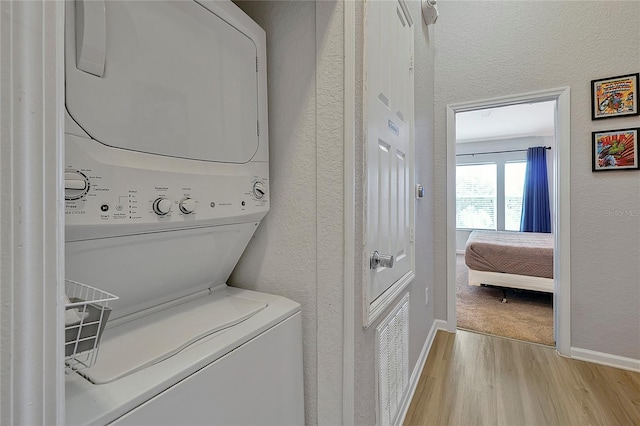 laundry room with stacked washer / drying machine and light hardwood / wood-style floors