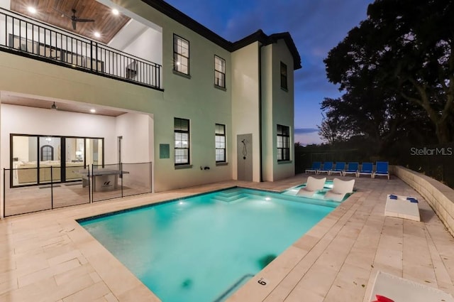 pool at dusk featuring ceiling fan and a patio area