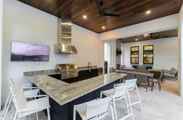 kitchen featuring a kitchen breakfast bar, ceiling fan, kitchen peninsula, wall chimney range hood, and wooden ceiling