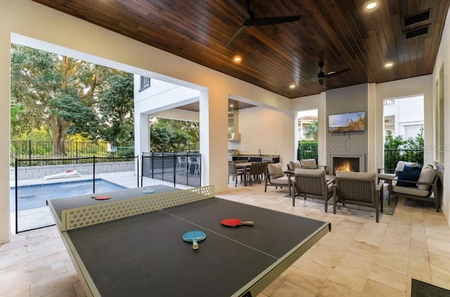 game room featuring a large fireplace, wooden ceiling, and ceiling fan