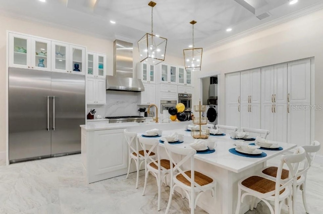 kitchen featuring decorative light fixtures, a kitchen breakfast bar, a large island, stainless steel appliances, and wall chimney exhaust hood