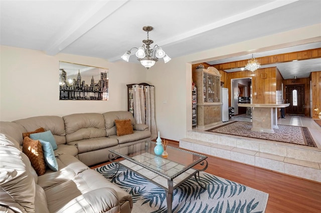 living room featuring an inviting chandelier, beam ceiling, light hardwood / wood-style floors, and wood walls