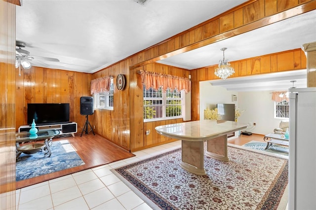 kitchen with light tile patterned flooring, ceiling fan with notable chandelier, decorative light fixtures, wood walls, and ornamental molding