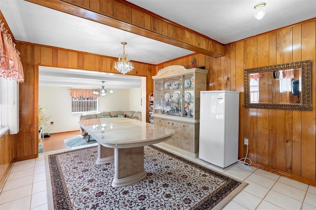 kitchen featuring light tile patterned flooring, pendant lighting, wood walls, white fridge, and a notable chandelier