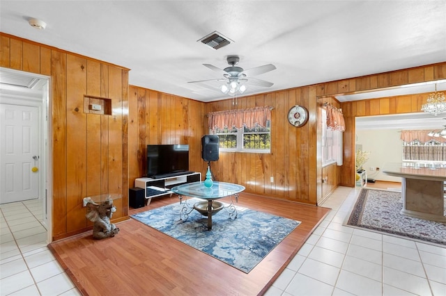 tiled living room with ceiling fan with notable chandelier and wood walls