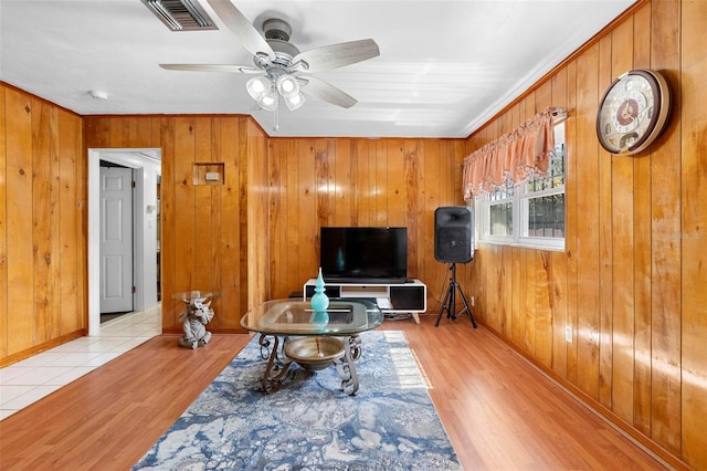 living room featuring ceiling fan, light hardwood / wood-style floors, and wood walls