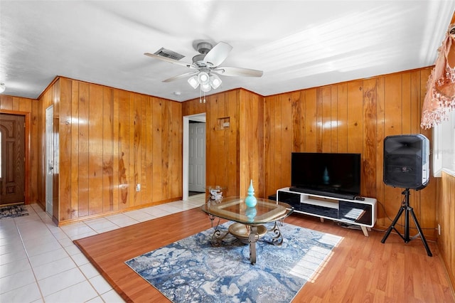 tiled living room featuring ceiling fan and wood walls