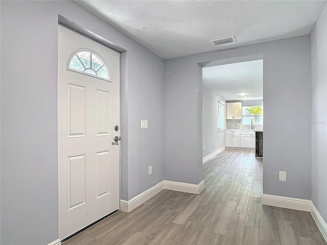 entrance foyer with light wood finished floors, visible vents, baseboards, and a textured ceiling