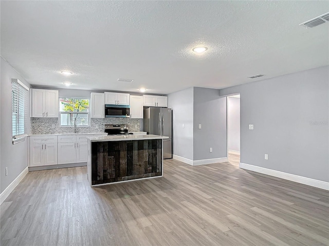 kitchen featuring decorative backsplash, appliances with stainless steel finishes, a center island, light countertops, and light wood-style floors