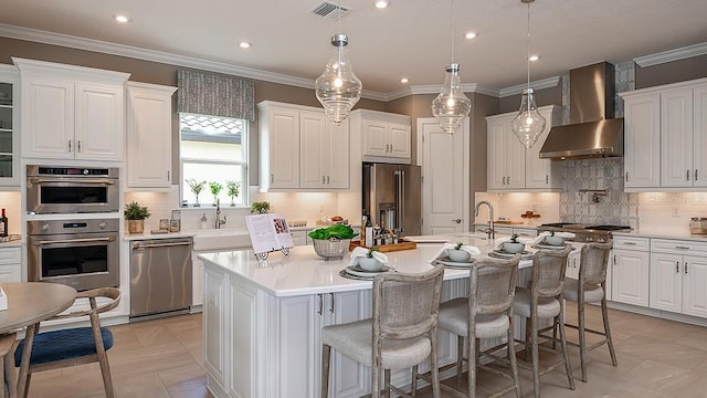 kitchen with stainless steel appliances, an island with sink, white cabinetry, and wall chimney exhaust hood