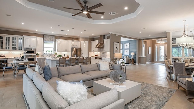 living room featuring wine cooler, ornamental molding, a raised ceiling, and ceiling fan with notable chandelier