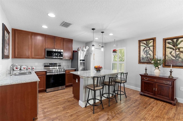 kitchen with appliances with stainless steel finishes, pendant lighting, sink, a center island, and light stone counters