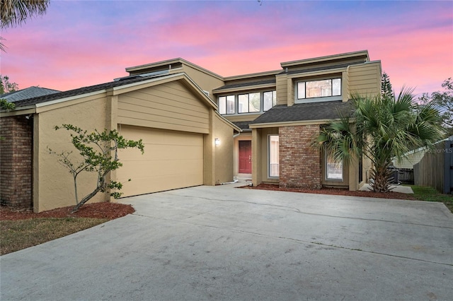 view of front of home featuring stucco siding, driveway, roof with shingles, a garage, and brick siding