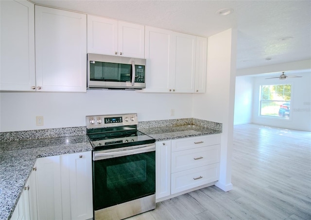 kitchen with appliances with stainless steel finishes, white cabinetry, ceiling fan, light stone counters, and light hardwood / wood-style flooring