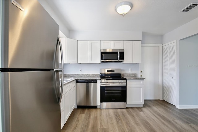 kitchen featuring white cabinetry, stainless steel appliances, light stone counters, and light wood-type flooring