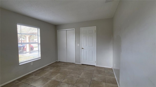 unfurnished bedroom featuring a closet, a textured ceiling, and light tile patterned floors