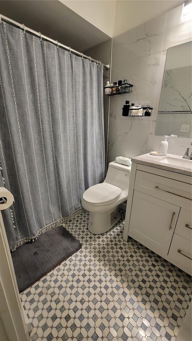 bathroom featuring vanity, toilet, and tile walls