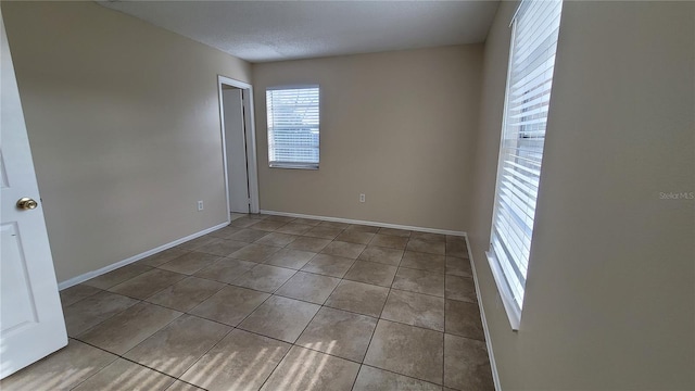 tiled empty room with a textured ceiling and baseboards