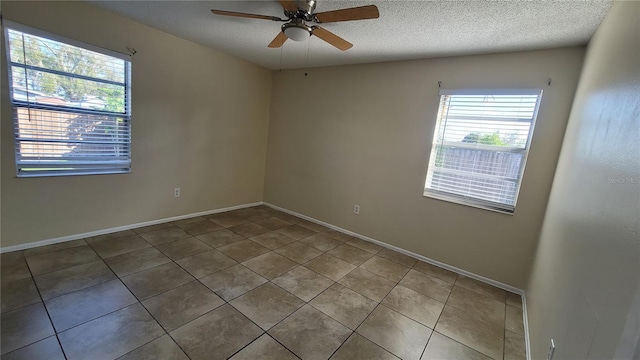 unfurnished room with a textured ceiling, ceiling fan, tile patterned floors, and baseboards