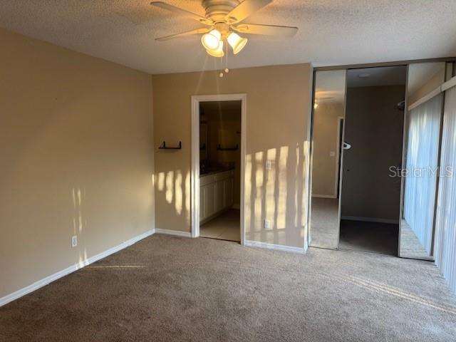 unfurnished bedroom with connected bathroom, a textured ceiling, carpet flooring, a closet, and ceiling fan