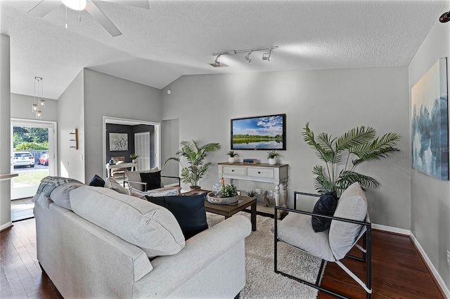 living room featuring vaulted ceiling, ceiling fan, dark wood-type flooring, track lighting, and a textured ceiling