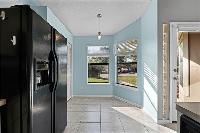 kitchen with hanging light fixtures, black fridge, light tile patterned floors, and a textured ceiling