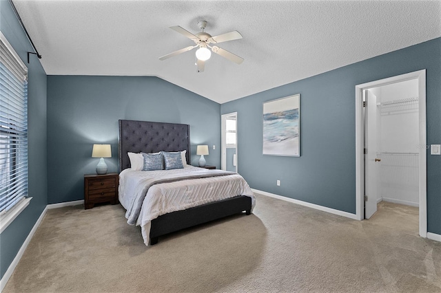 carpeted bedroom with vaulted ceiling, a spacious closet, a textured ceiling, and ceiling fan