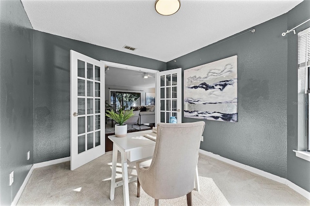 dining space with ceiling fan, light colored carpet, french doors, and a textured ceiling