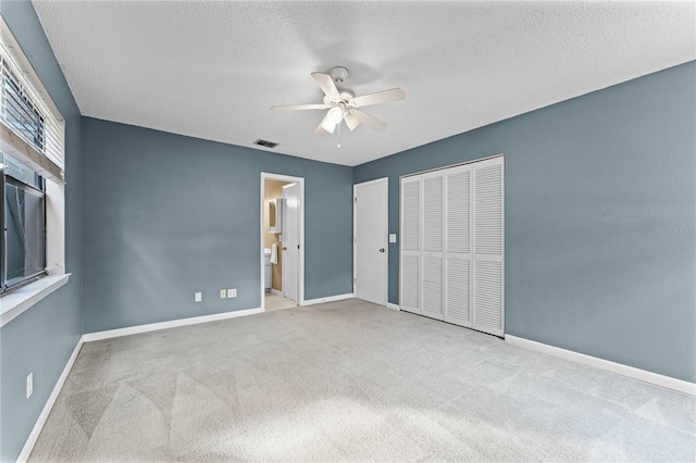 unfurnished bedroom with ensuite bathroom, light colored carpet, ceiling fan, a textured ceiling, and a closet