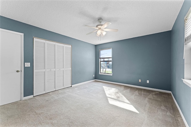 unfurnished bedroom with ceiling fan, light colored carpet, a textured ceiling, and a closet