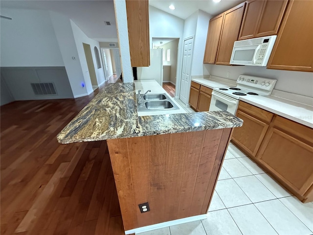 kitchen with sink, stone countertops, vaulted ceiling, white appliances, and light hardwood / wood-style floors