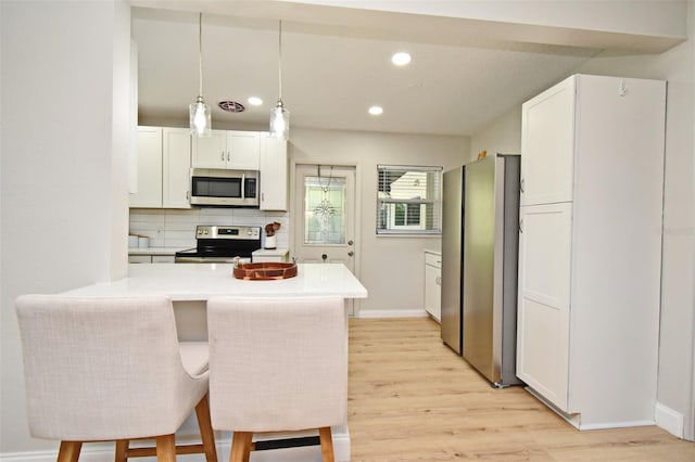 kitchen featuring a breakfast bar area, decorative light fixtures, kitchen peninsula, stainless steel appliances, and white cabinets