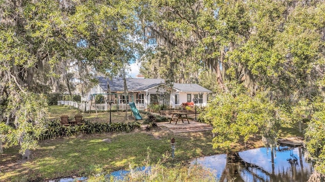 rear view of house featuring a playground, a water view, and a lawn