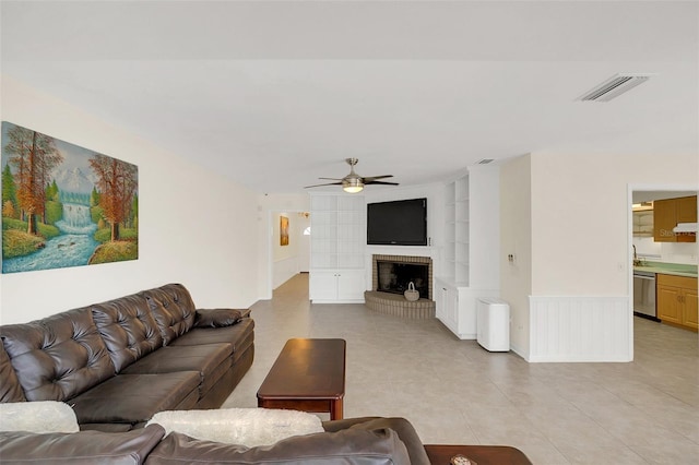 tiled living room with a brick fireplace, built in features, and ceiling fan