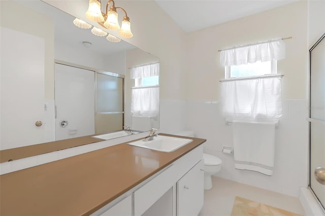 bathroom featuring a shower with door, an inviting chandelier, tile walls, vanity, and toilet