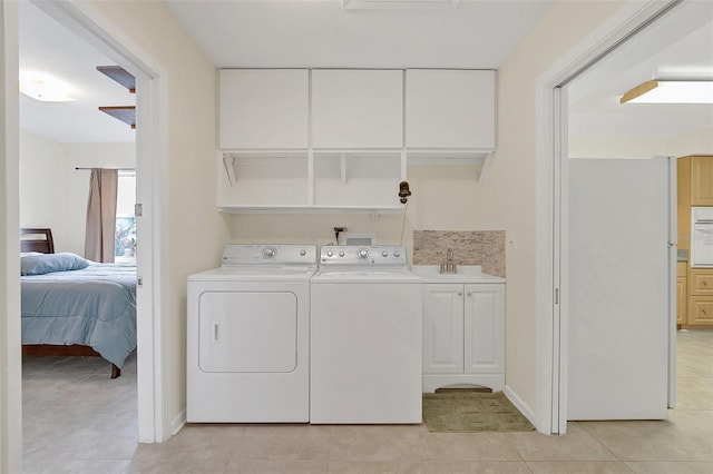 clothes washing area with cabinets, sink, light tile patterned floors, and washing machine and clothes dryer