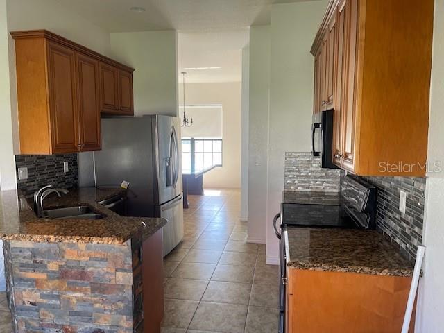 kitchen featuring light tile patterned flooring, sink, tasteful backsplash, range, and dark stone countertops