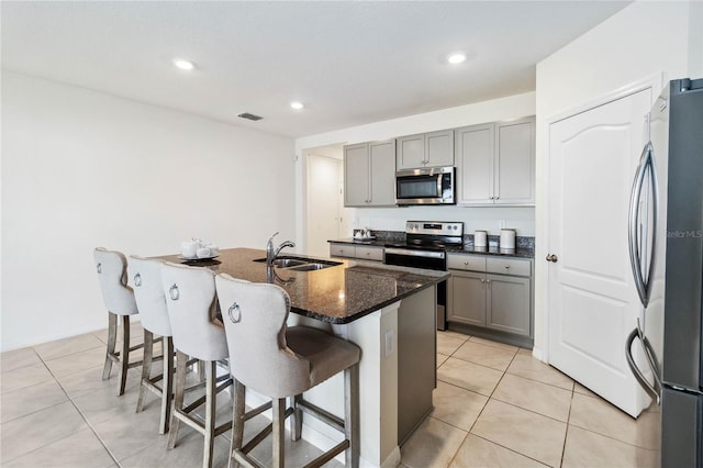 kitchen featuring sink, gray cabinetry, dark stone counters, a kitchen island with sink, and stainless steel appliances