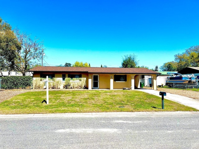 ranch-style house featuring concrete driveway, a front lawn, an attached carport, and stucco siding