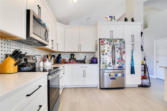 kitchen featuring decorative backsplash, vaulted ceiling, stainless steel appliances, light countertops, and white cabinetry